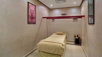 A small, private room with a single bed, a small table with a bottle and a cup, and a framed picture on the wall.
