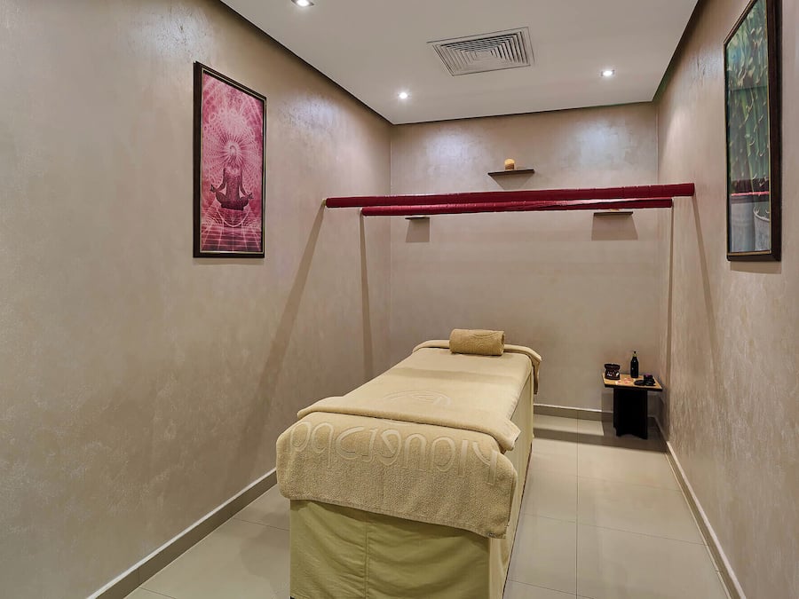 A small, private room with a single bed, a small table with a bottle and a cup, and a framed picture on the wall.