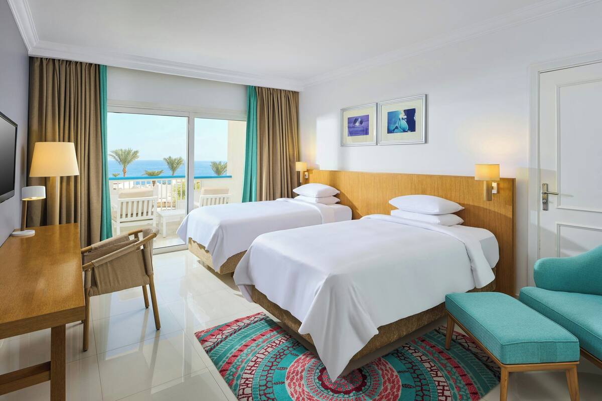 Une chambre d’hôtel avec deux lits, un bureau, une chaise, un canapé et une vue sur la mer.