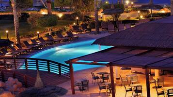 A pool area with lounge chairs and umbrellas, surrounded by palm trees and a view of the ocean.