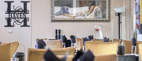 A dining area with wicker chairs, a table set with a wine glass, and a framed artwork above the table.
