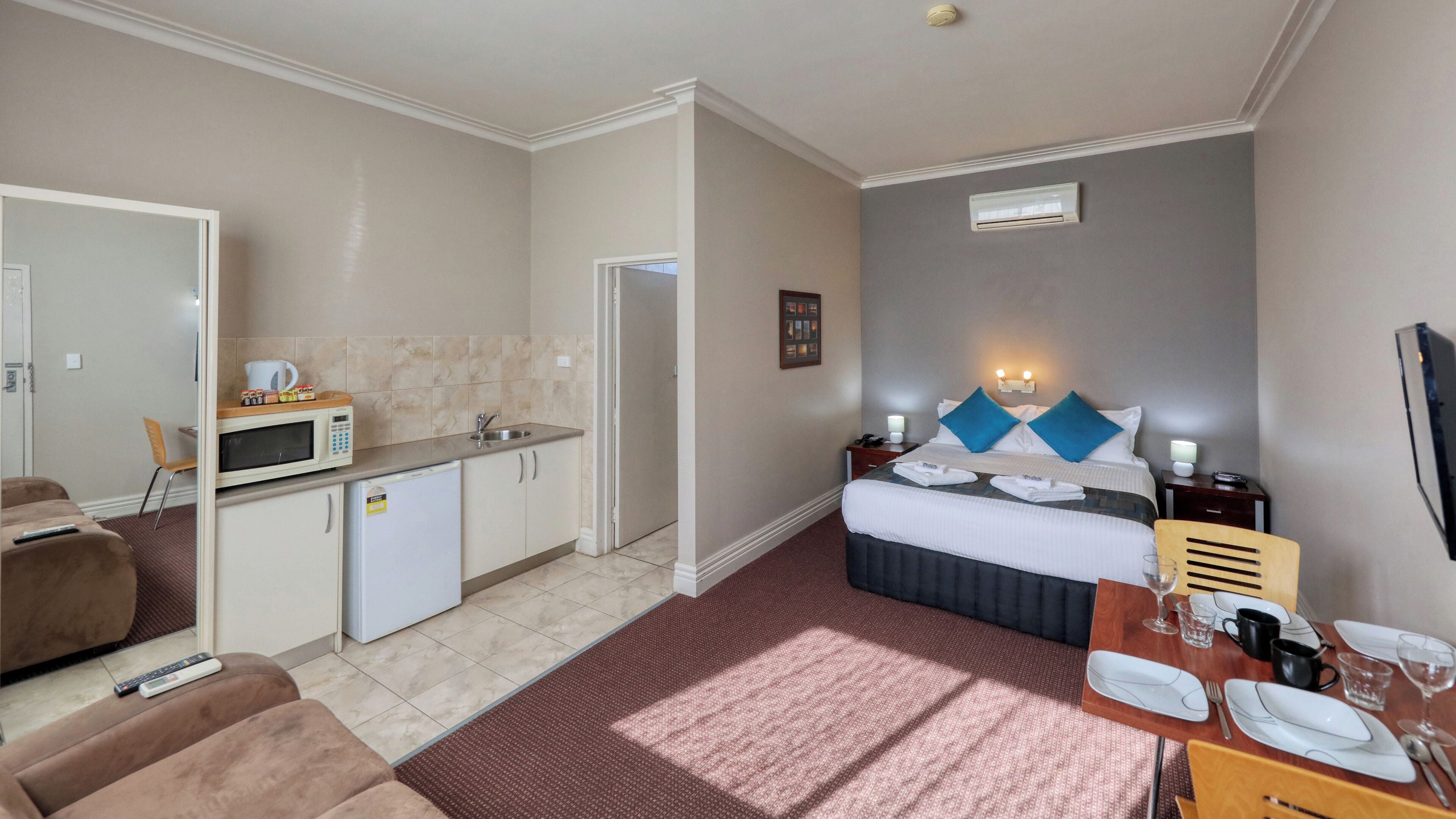 A hotel room with a bed, a small kitchenette, a dining area, and a living area.