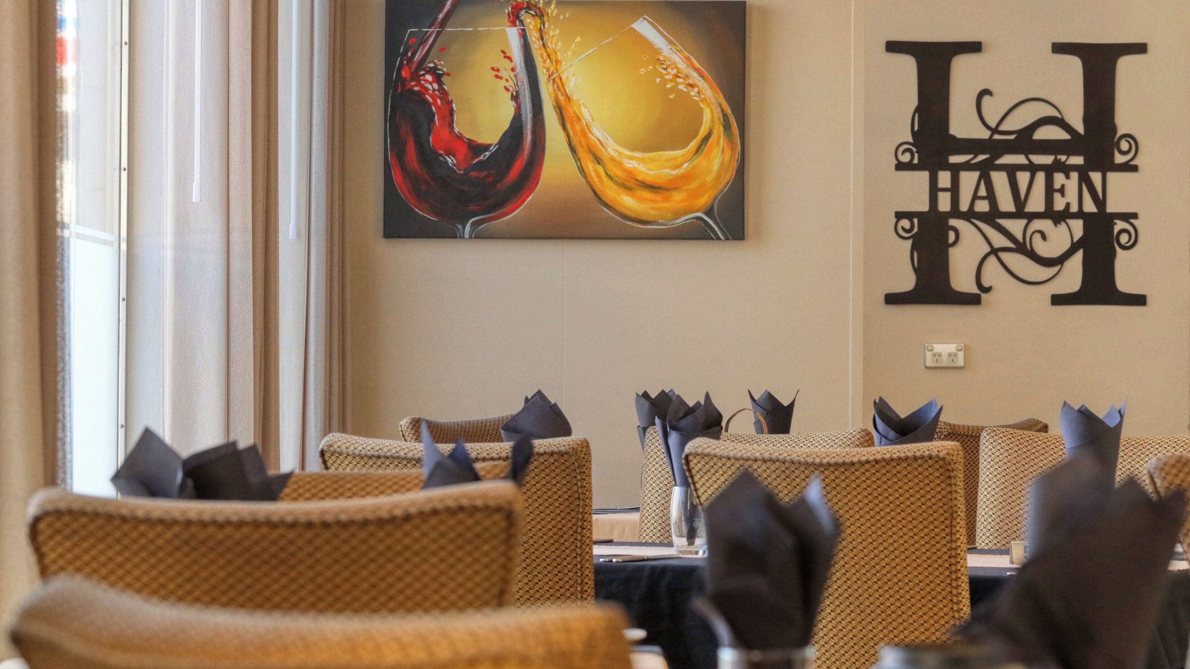 Interior de restaurant amb cadires de vimet, una taula amb un got de vi negre i una paret amb el rètol 'LI HAVEN'.