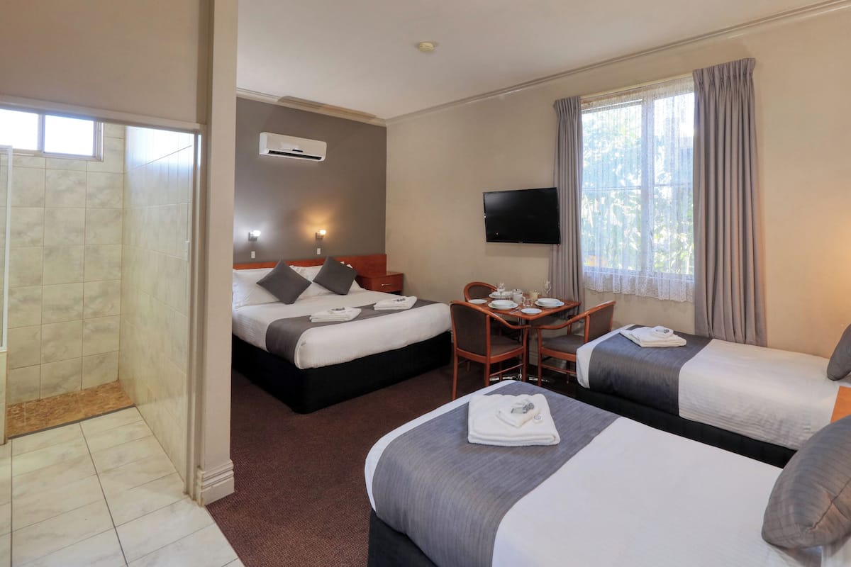 Ein Hotelzimmer mit zwei Betten, einem kleinen Tisch mit Stühlen, einem Fernseher und einem Fenster mit Vorhängen.
