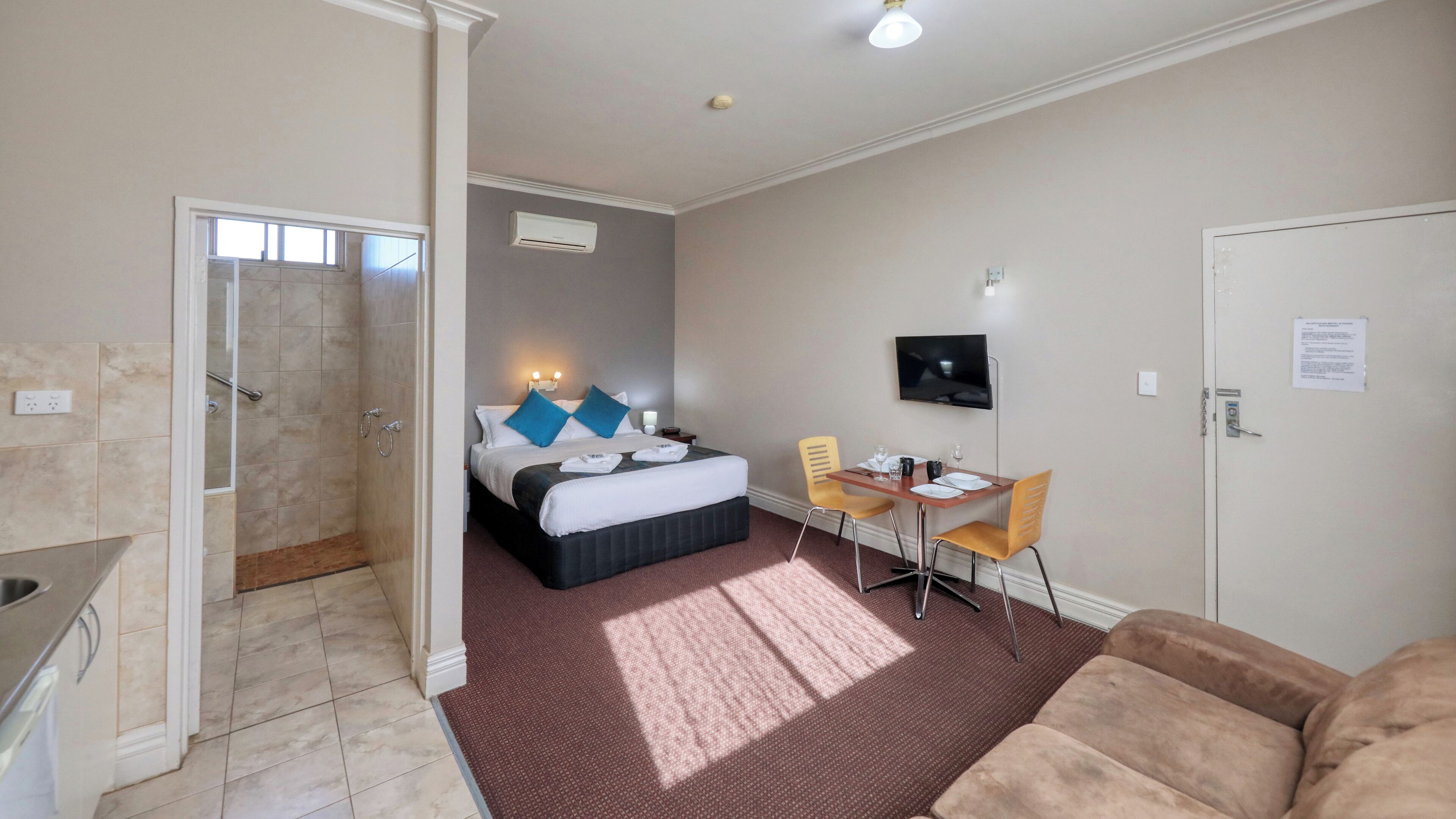 A hotel room with a bed, a desk with a chair, a TV, and a shower area.