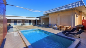A swimming pool with lounge chairs and a table, surrounded by a covered patio area with a tiled floor. - Silver Haven Motor Inn (Broken Hill)
