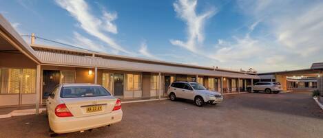 Un motel con una hilera de habitaciones, una zona de estacionamiento techada y cielo despejado.