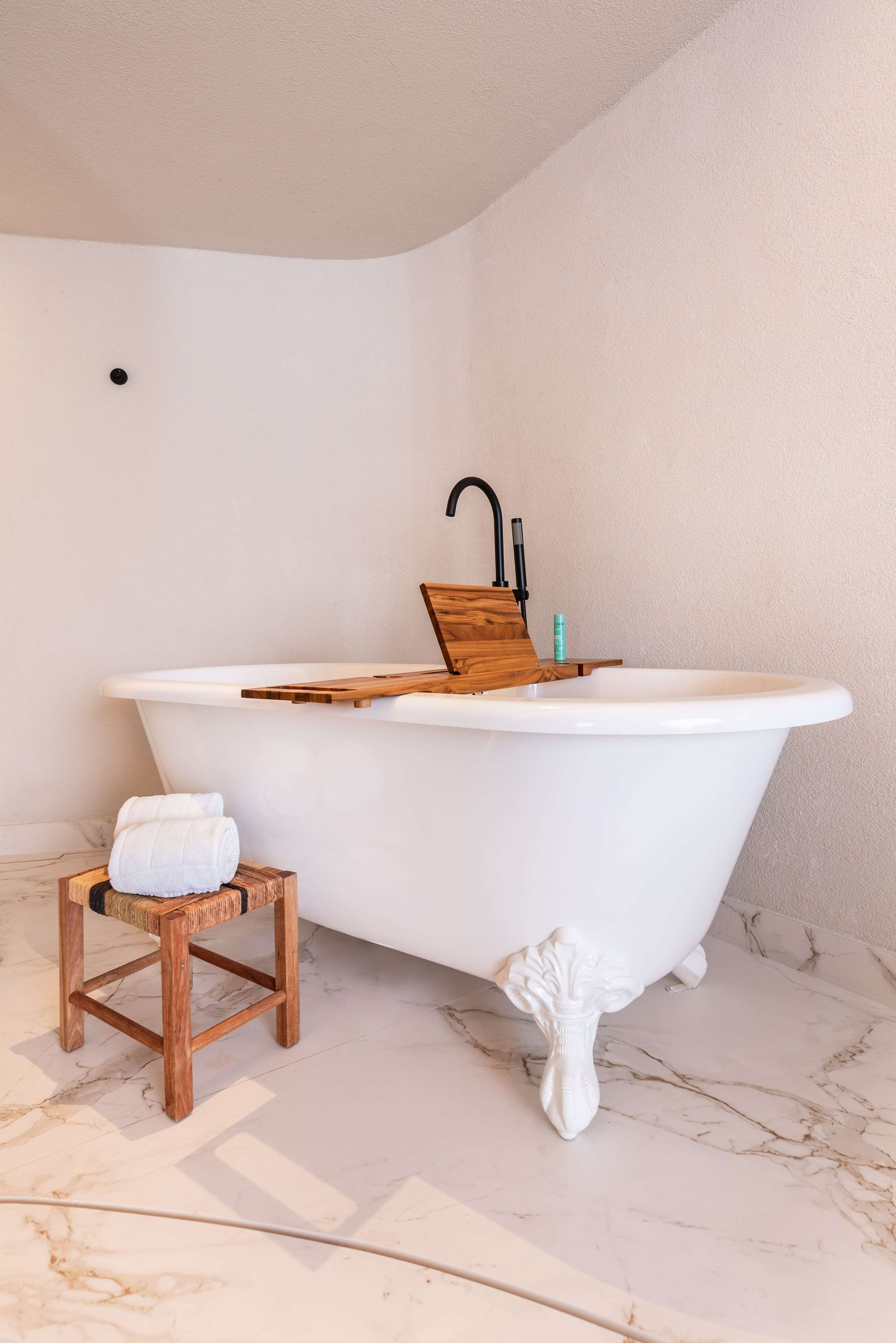 Un baño con una bañera independiente, un taburete de madera y un pequeño estante de madera.