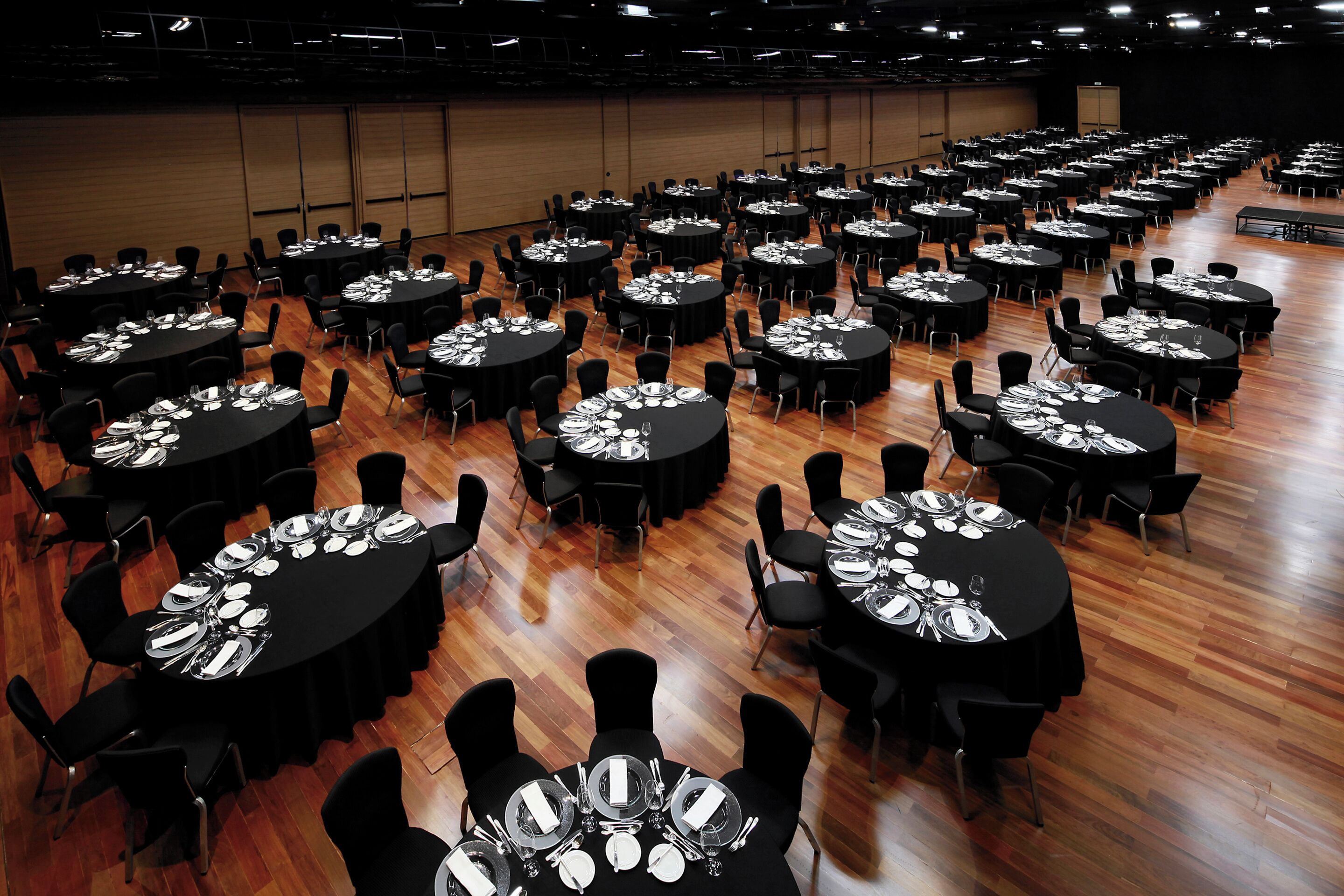 A large conference room with multiple round tables, each set with plates, cutlery, and glasses.