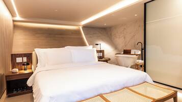 A modern bedroom with a large bed, bedside tables, a nightstand, a wooden bench, and a glass partition.