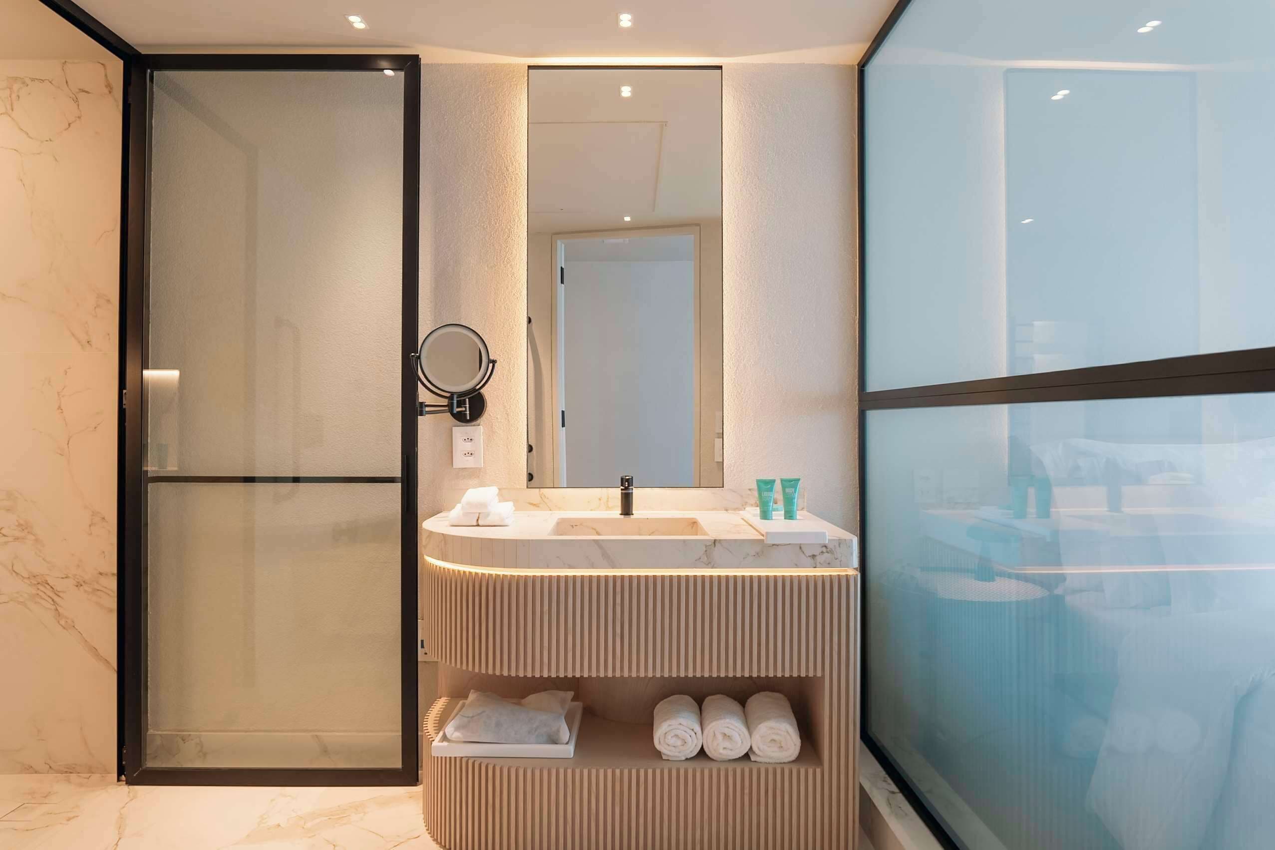 A modern bathroom with a glass shower enclosure, a marble-topped sink, and a large mirror.