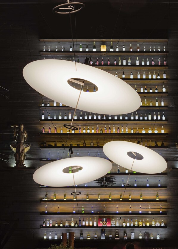 A bar with multiple shelves of liquor bottles and three large, oval-shaped hanging light fixtures.