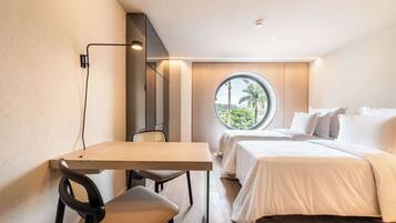 Quarto de hotel moderno com escrivaninha de madeira, duas camas, janela redonda com vista para palmeiras e luminária fixada na parede.