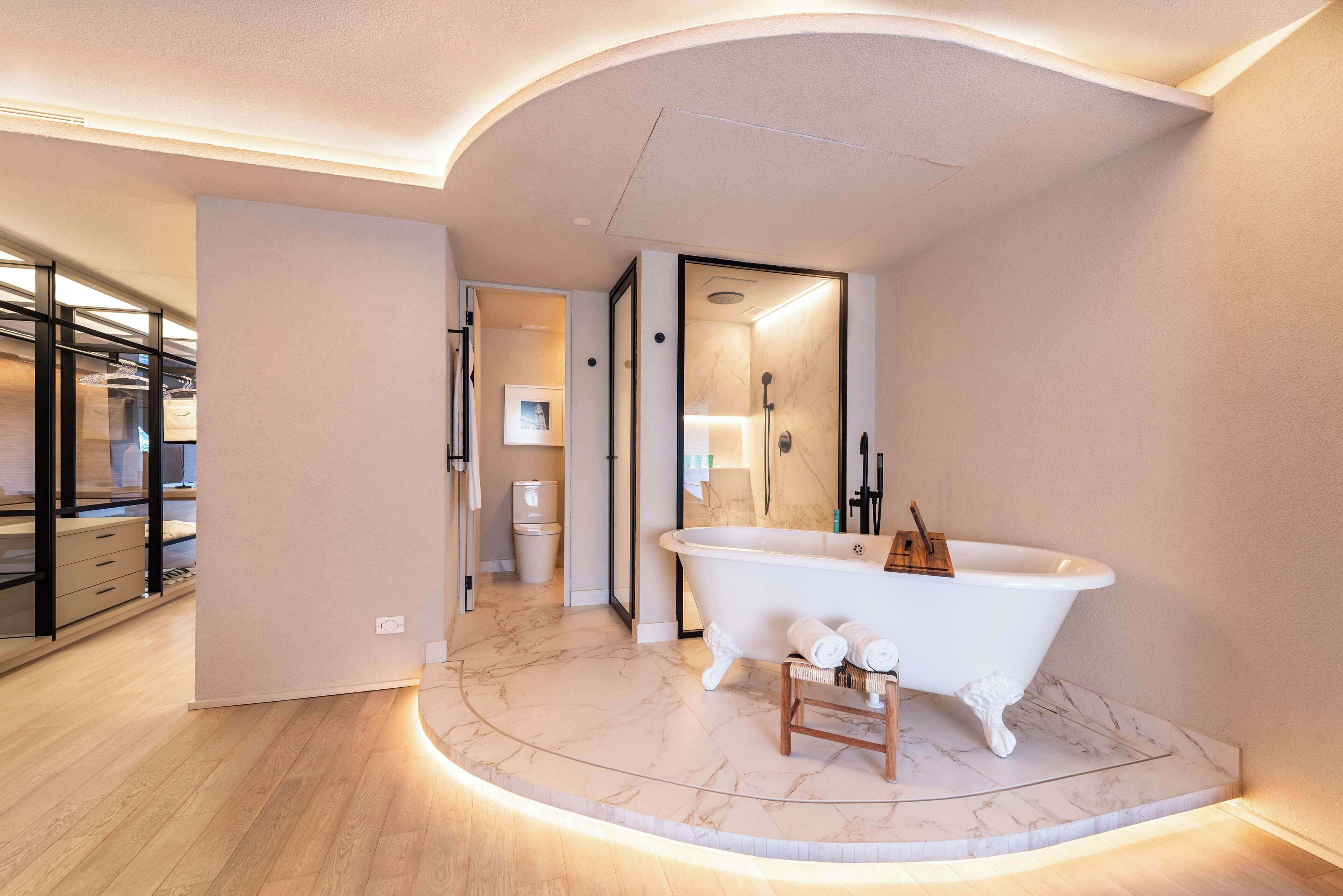A modern bathroom with a freestanding bathtub, wooden stool, and marble flooring.
