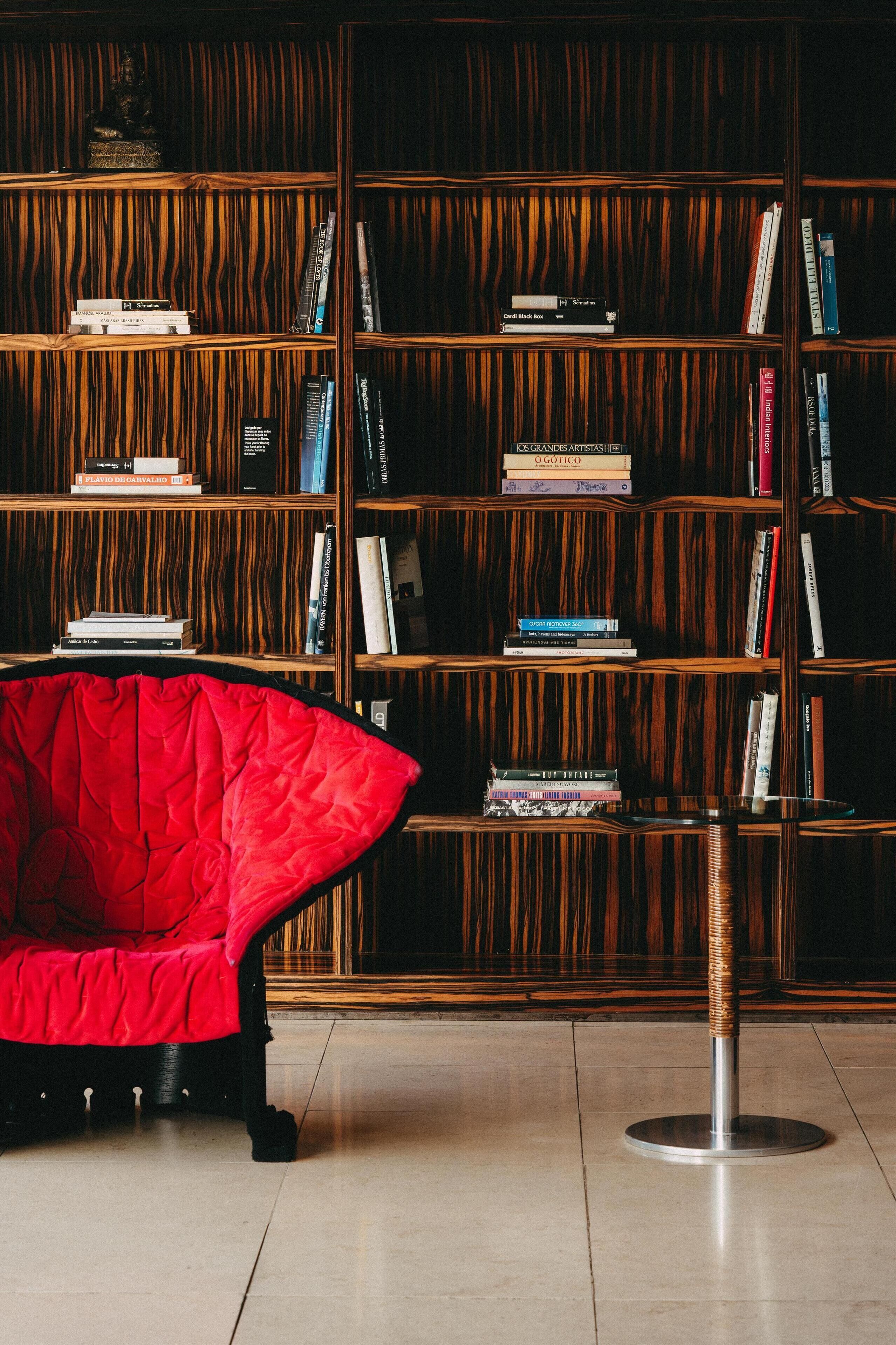 Una habitación con una estantería, una silla roja y una mesa redonda.