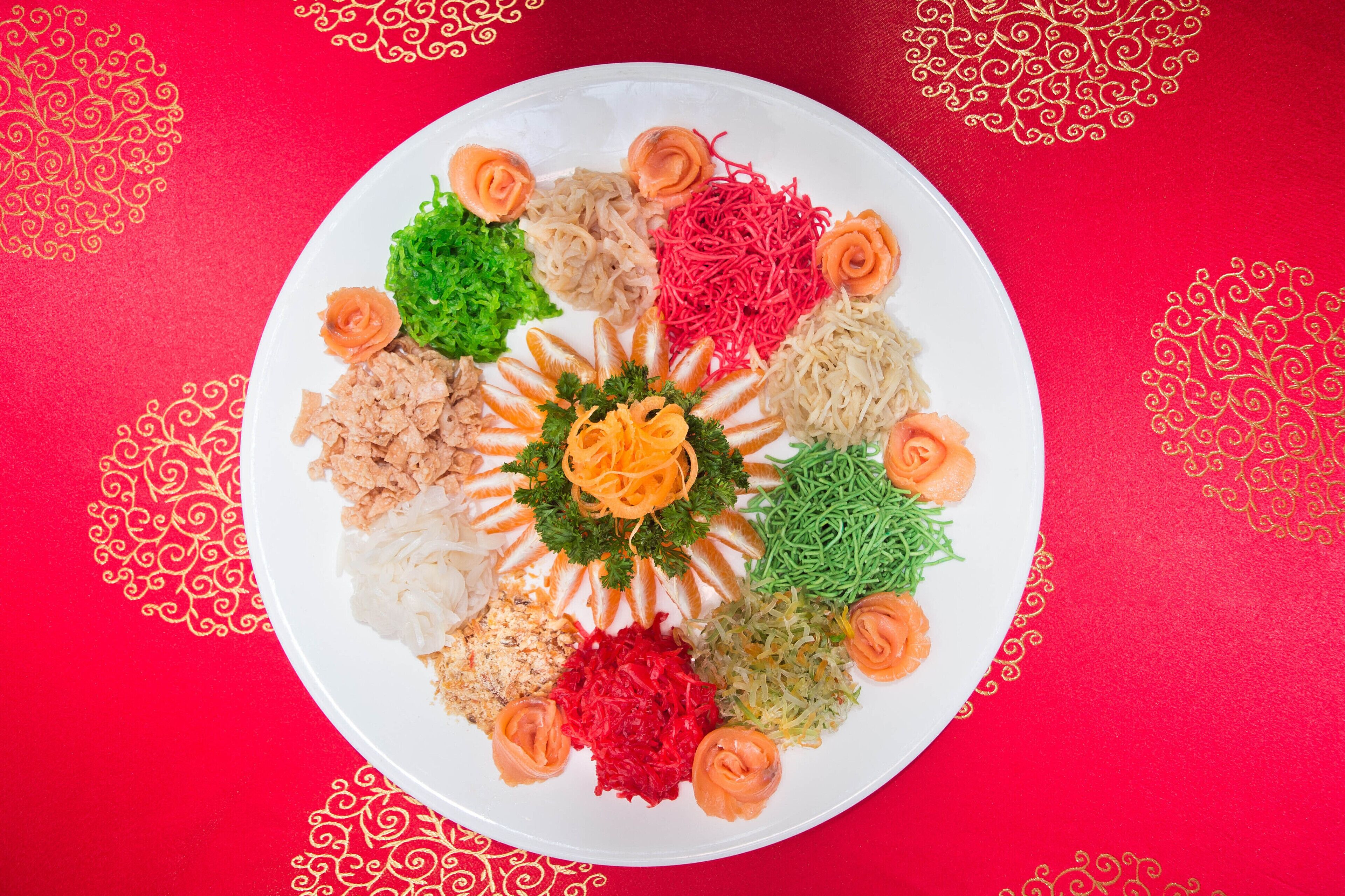 A white plate with various food items arranged in a circular pattern on a red background with gold designs.
