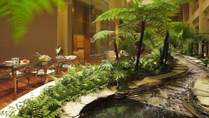 Rebost d'hotel amb una font, plantes d'interior i zona de dinar amb taules i cadires.