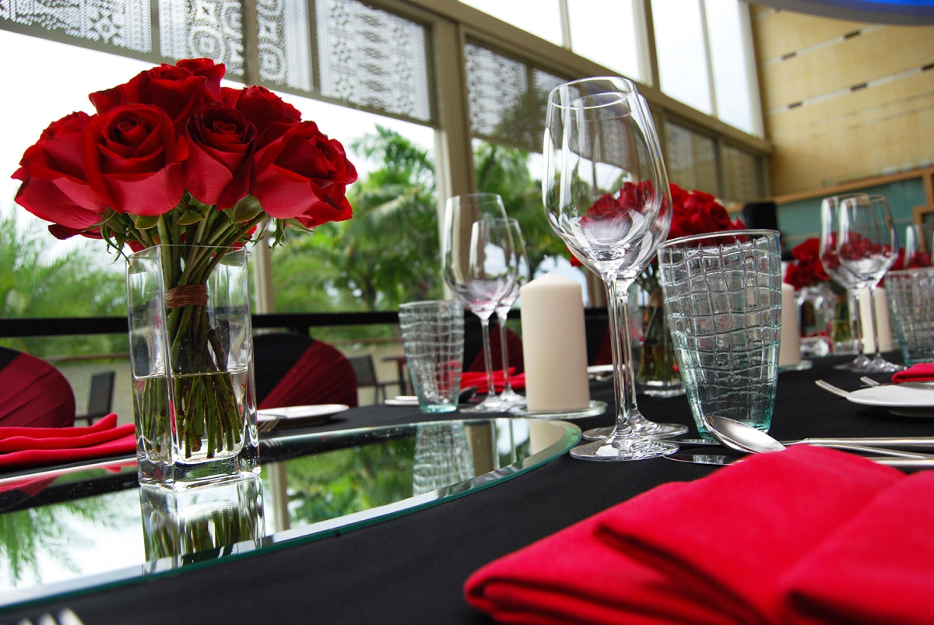 A table set for dining with clear glassware, a vase of red roses, and a candle.