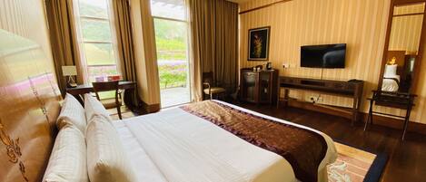 A hotel room with a large bed, a desk, a chair, a TV, and a view of the outdoors.