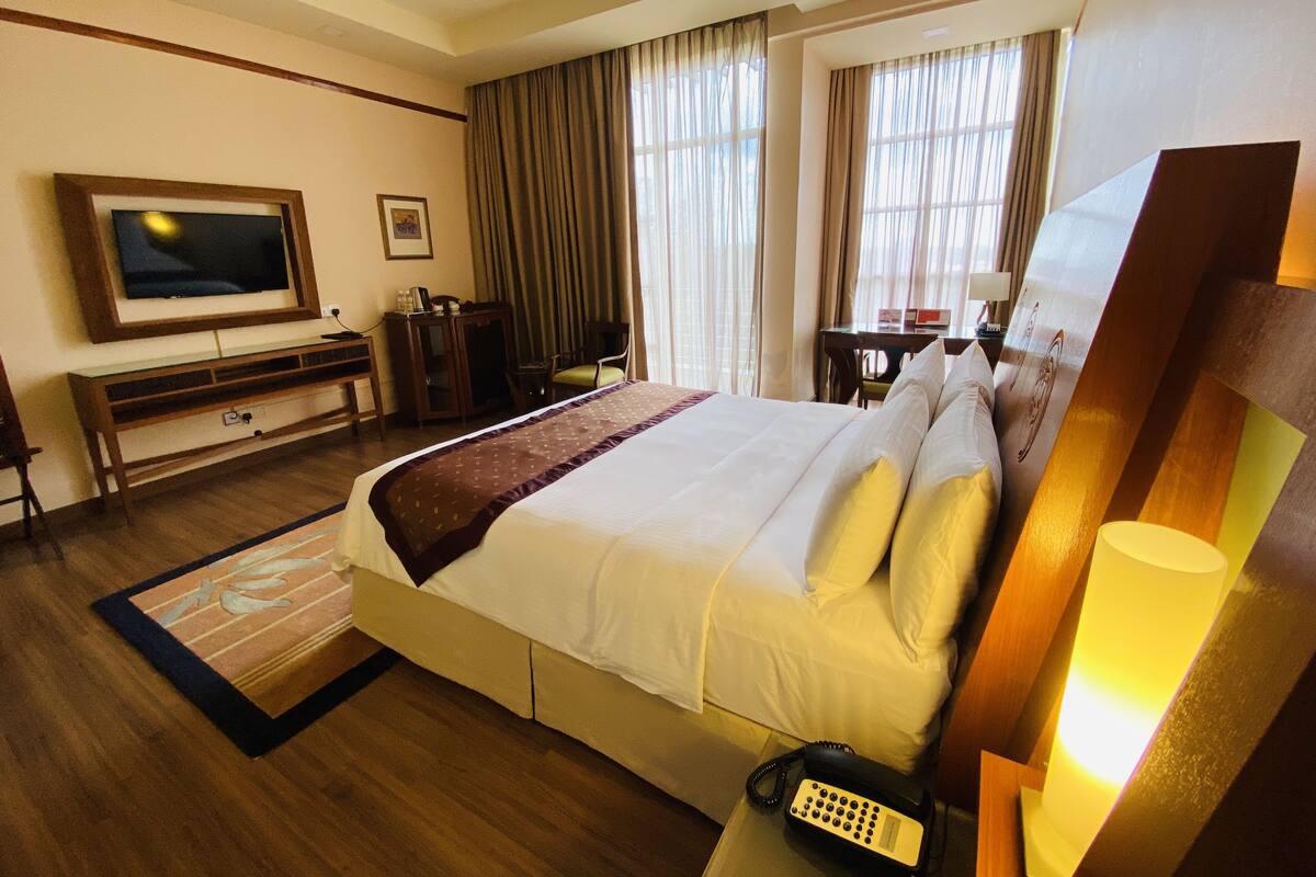 A hotel room with a large bed, a television, a desk, and a telephone.