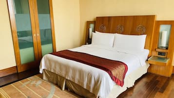 Habitación de hotel con una cama grande, cabecera de madera, lámparas de noche y una puerta de vidrio que da a un balcón.