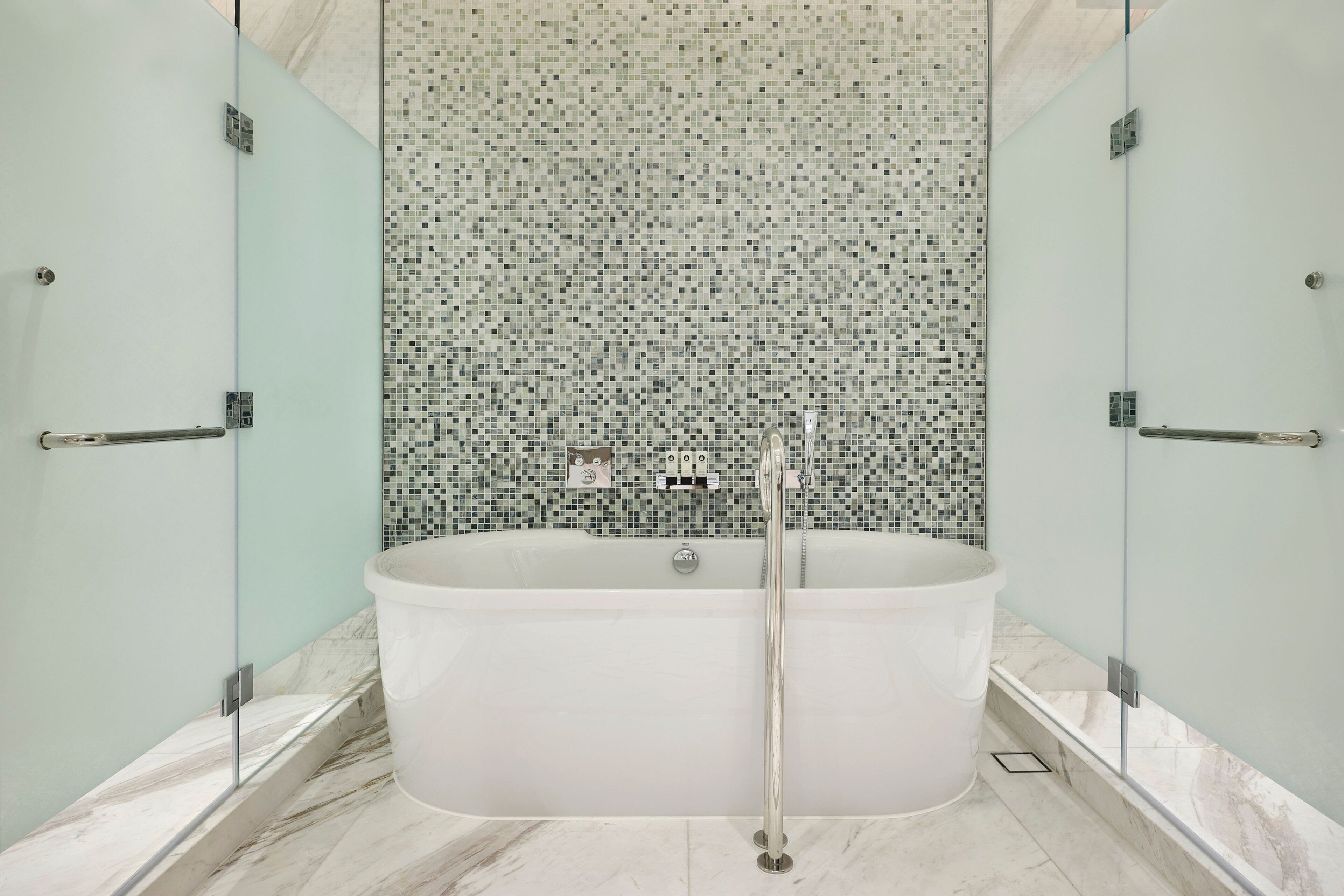 A modern bathroom with a freestanding bathtub, glass shower enclosure, and mosaic tile backsplash.