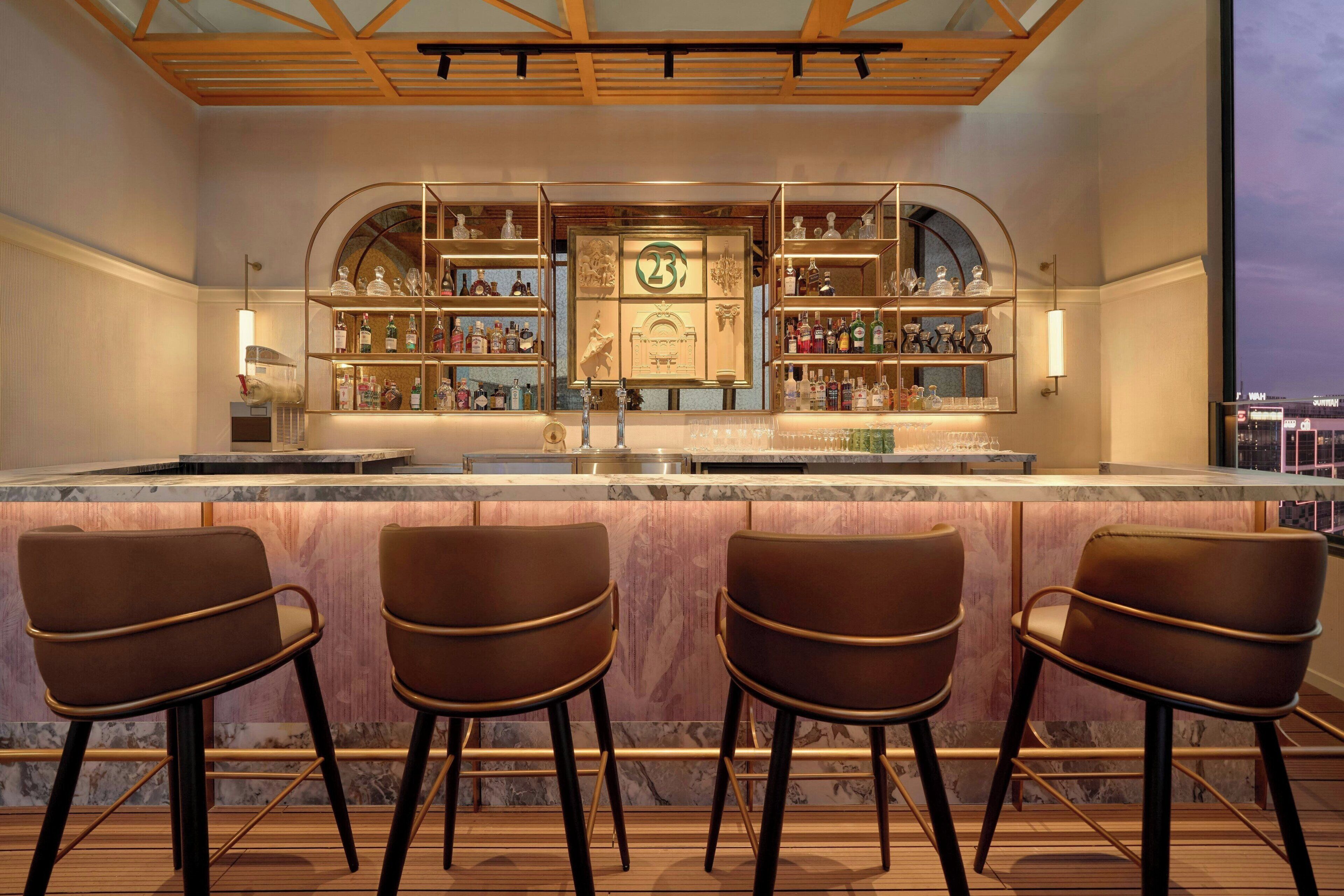 Eine Bar mit Marmorplatte, mehreren Regalen voller Spirituosenflaschen und drei Barhocker.