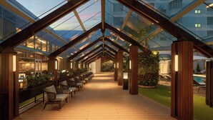 A covered outdoor area with wooden flooring, seating, and glass walls.