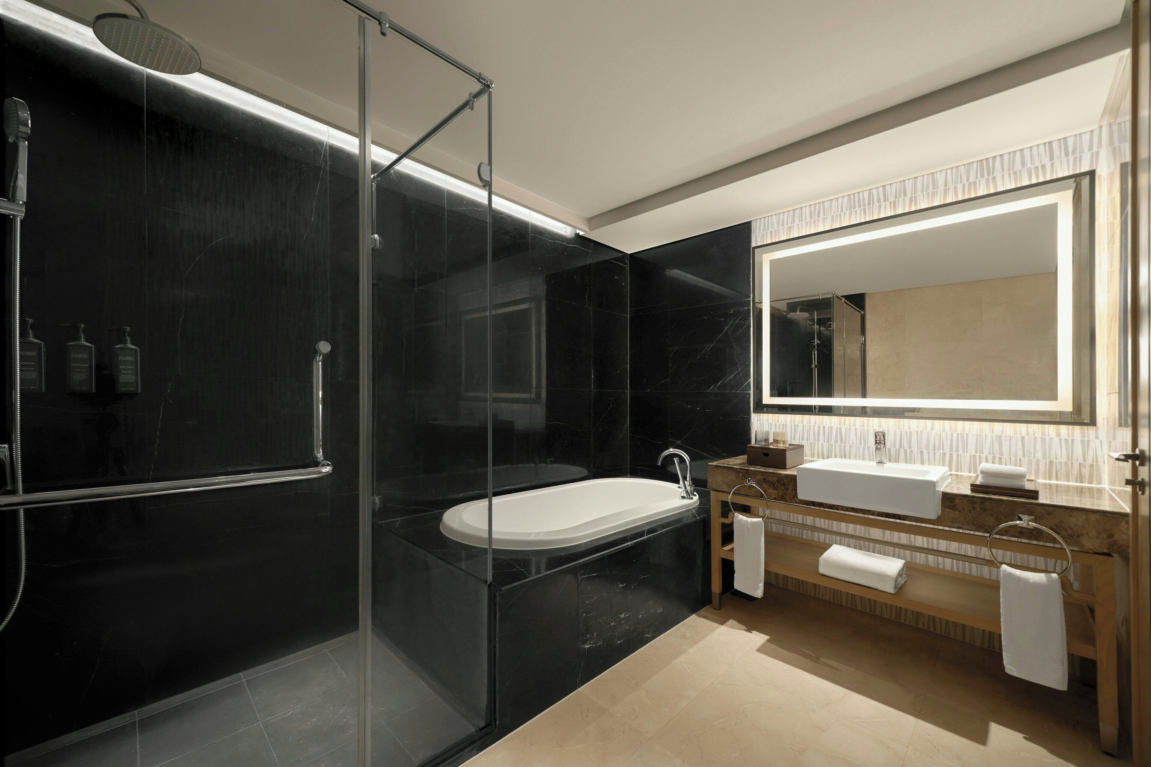 Un baño moderno con ducha de vidrio, una bañera independiente, un tocador con espejo y un lavamanos.