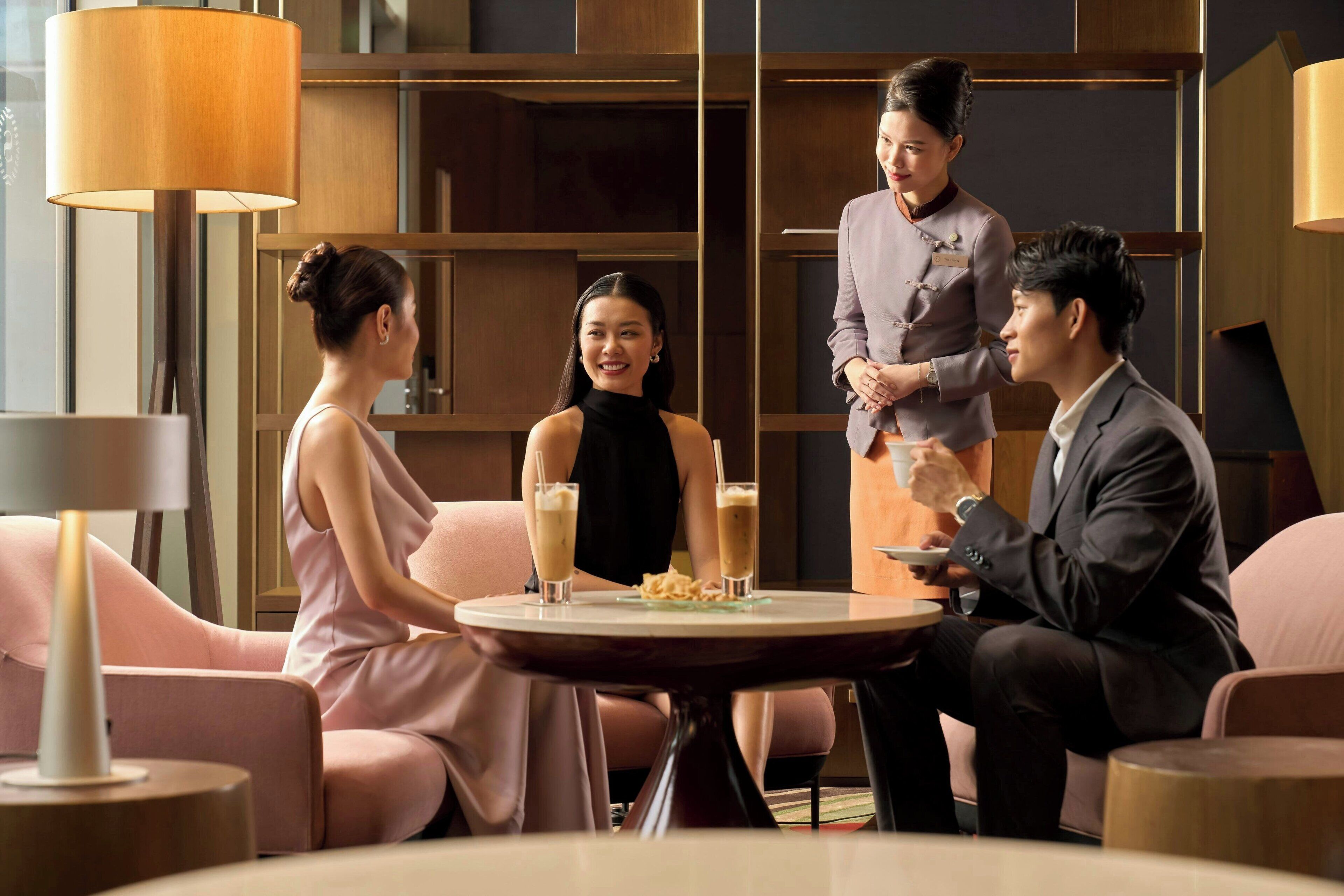 A modern hotel room with a round table, comfortable seating, and a large bookshelf.