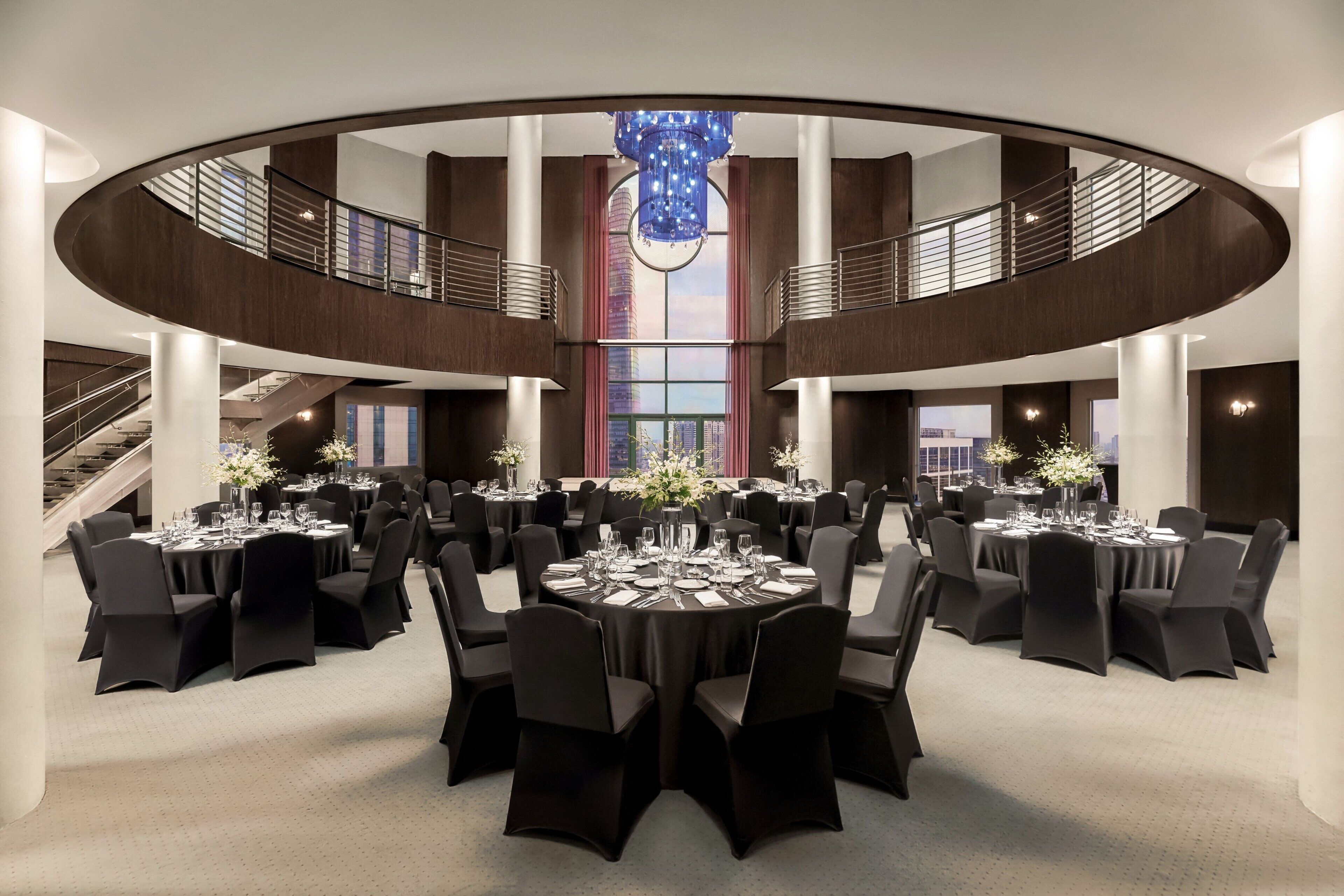 Een ruime, moderne hotellobby met een ronde centrale tafel, gedekt voor een formeel evenement, omringd door zwarte stoelen.