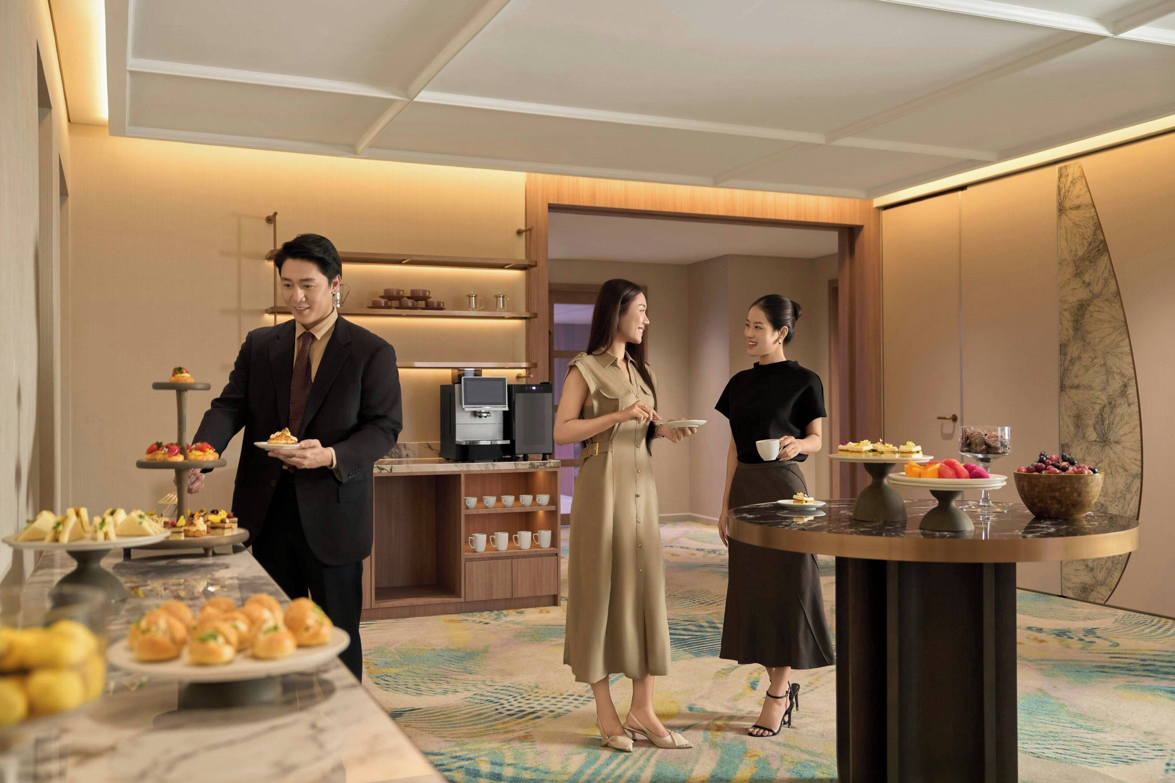 A hotel room with a dining area featuring a buffet table with various food items and a coffee machine.