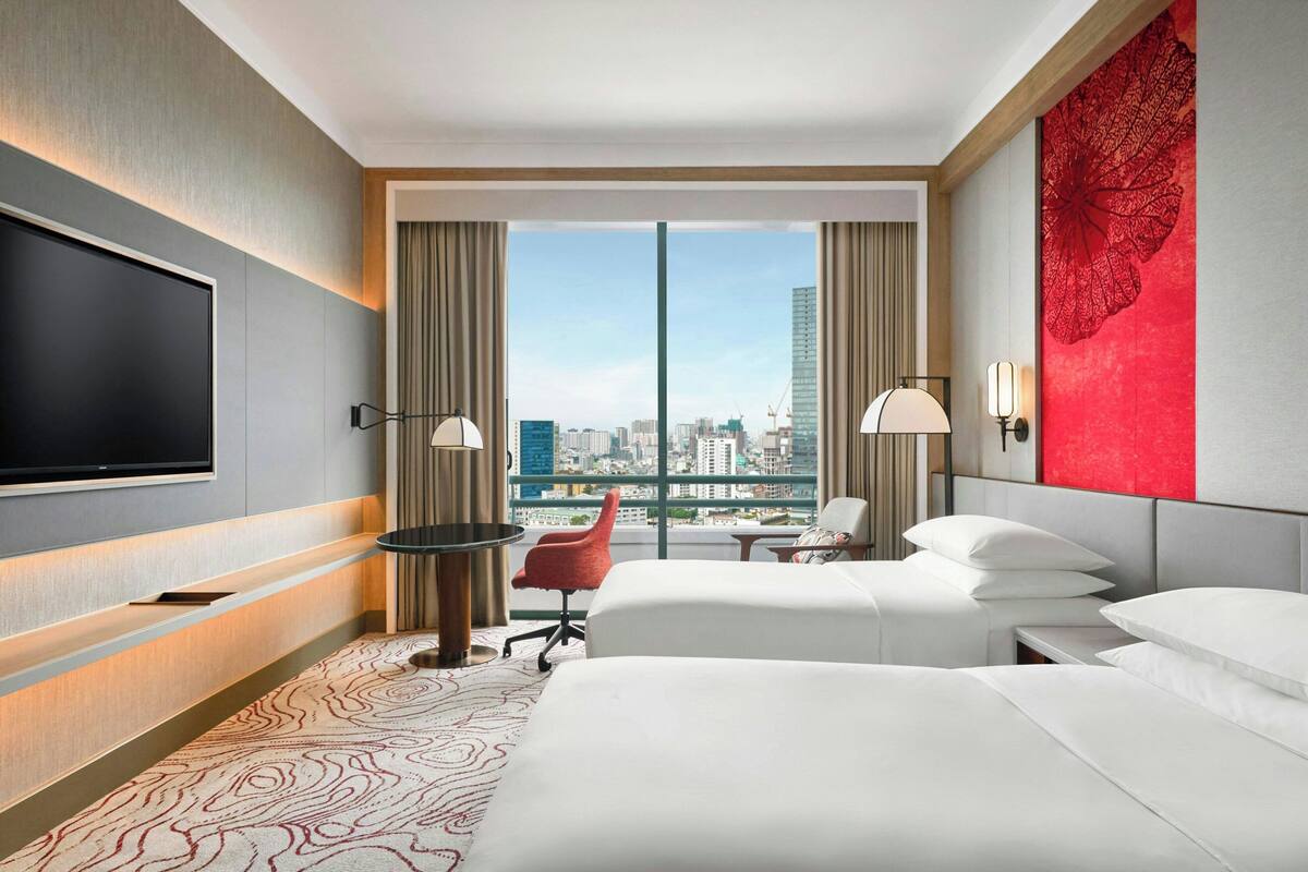 A hotel room with a large bed, a desk, a chair, a TV, and a view of the cityscape.