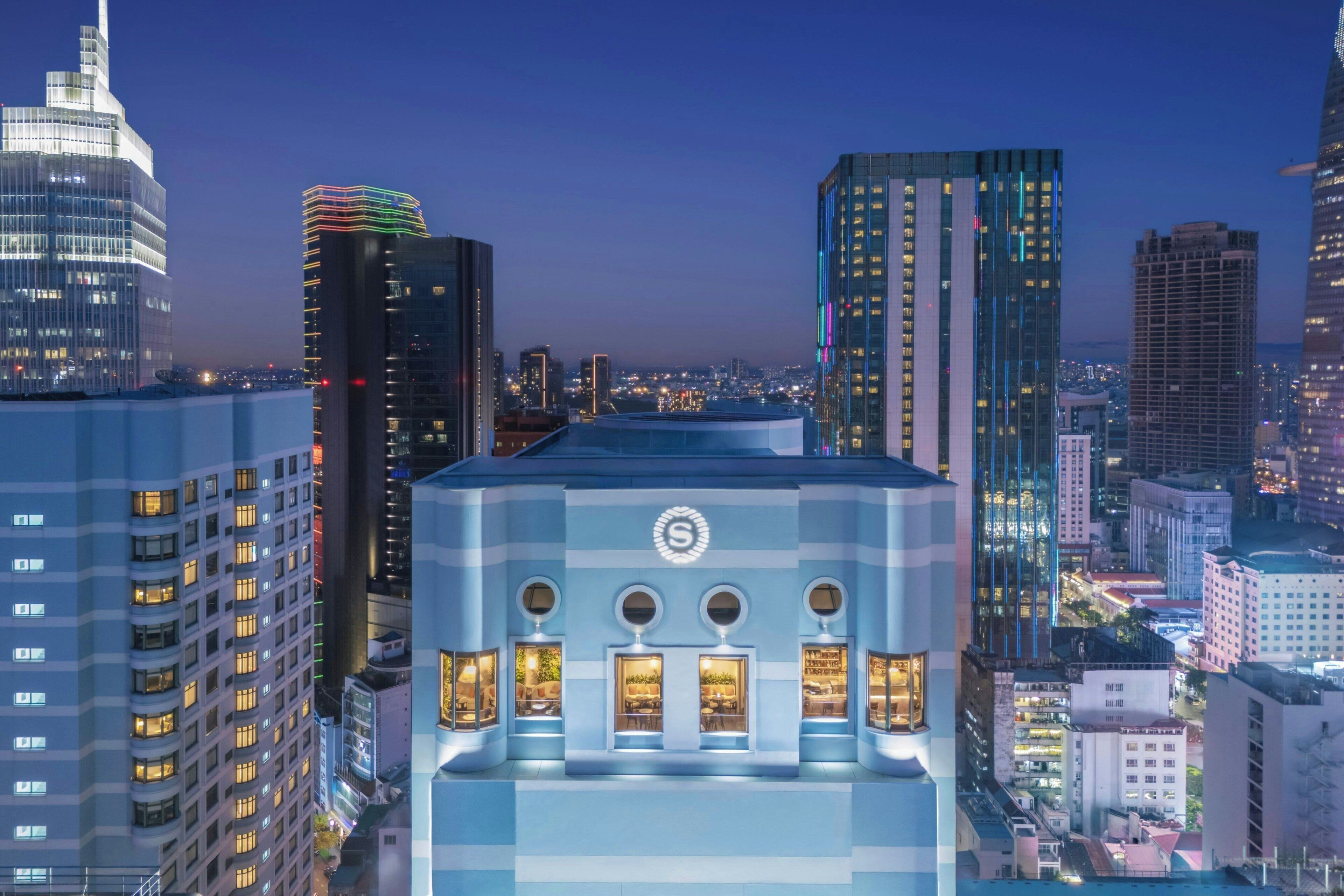 A modern building with a distinctive geometric facade and circular windows, surrounded by high-rise buildings in a cityscape.