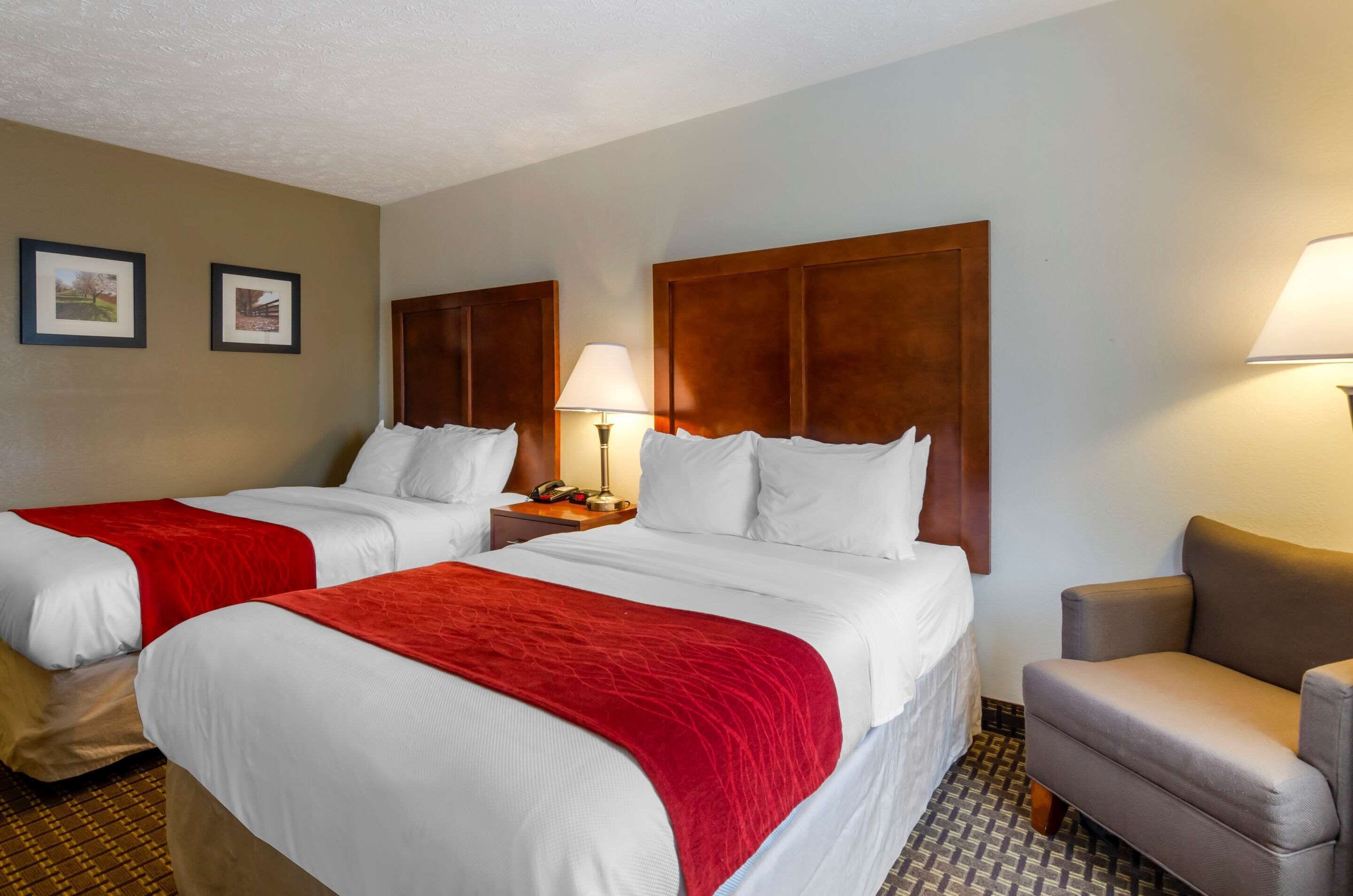 A hotel room with two beds, each with a red blanket, a wooden headboard, and a nightstand with a lamp.