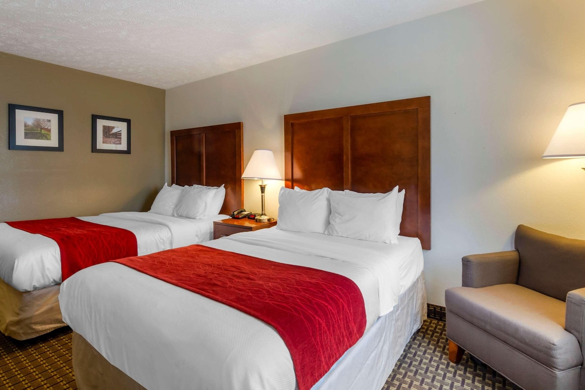 Une chambre d’hôtel avec deux lits, chacun recouvert d’une couverture rouge, dotée d’une tête de lit en bois et d’une table de chevet avec une lampe.