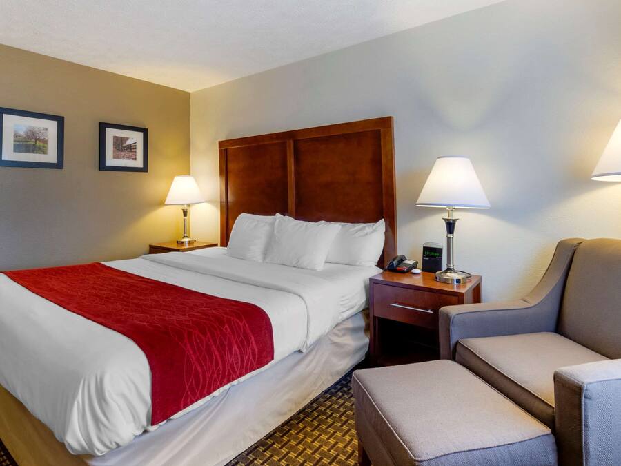 A hotel room with a large bed, two bedside lamps, a wooden headboard, and a small table with a phone and a lamp.