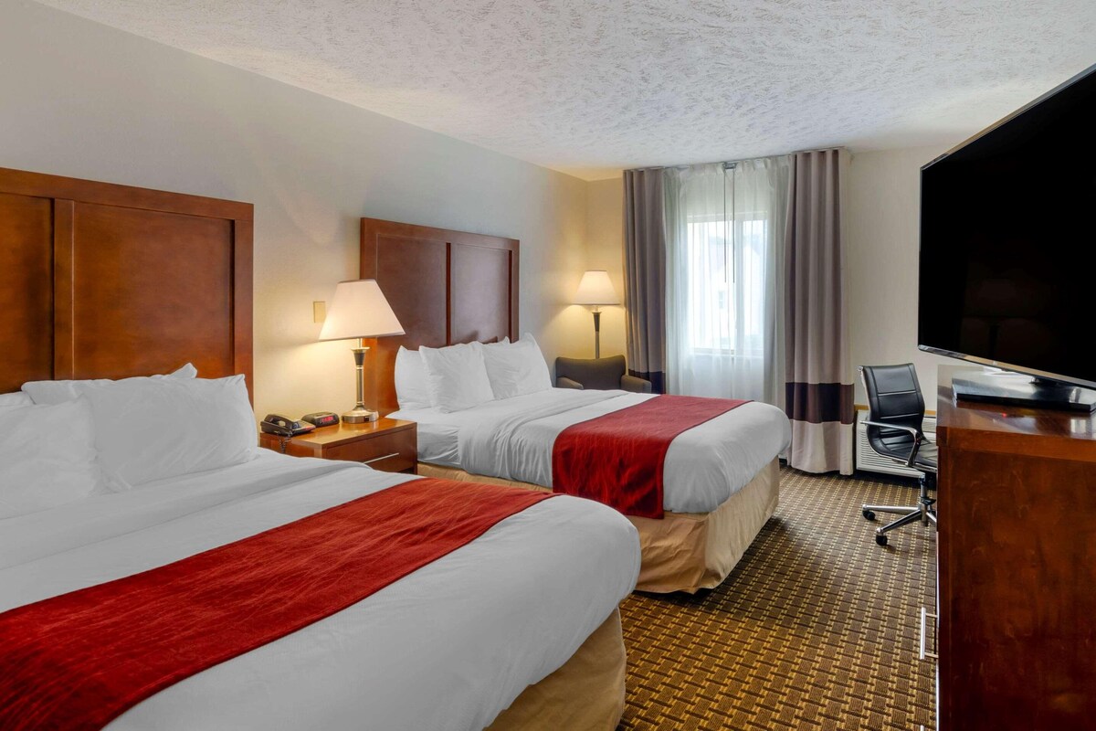 A hotel room with two beds, a desk, a TV, and a window with curtains.