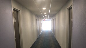 Un pasillo largo y estrecho con puertas a ambos lados, que conduce a una salida iluminada al final.