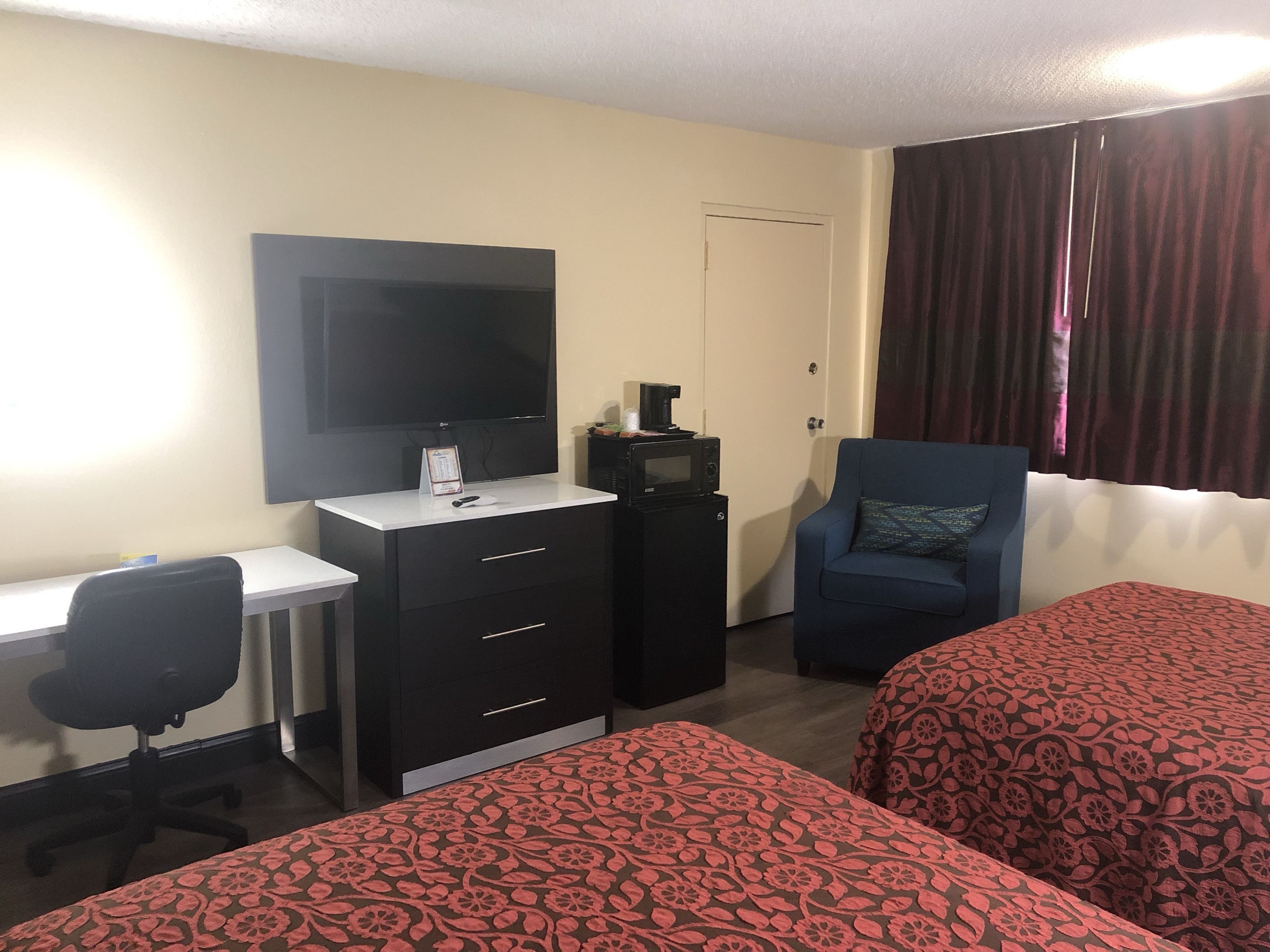 Habitación de hotel con escritorio, televisor, cafetera, microondas, una silla y dos camas con cubrecamas estampados.