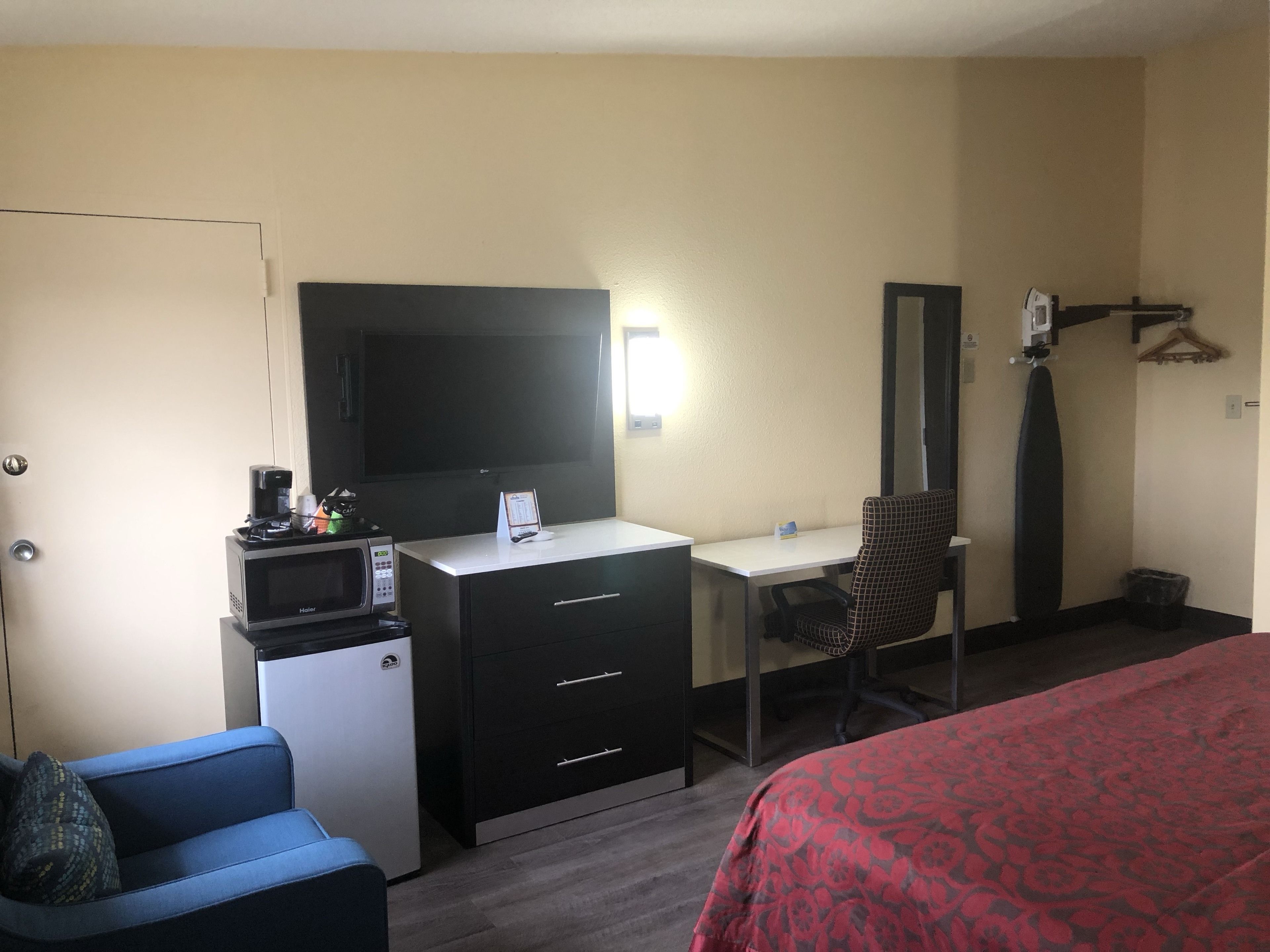 Une chambre d’hôtel équipée d’un bureau, d’une chaise, d’un lit, d’un four à micro-ondes, d’une télévision et d’un petit réfrigérateur.