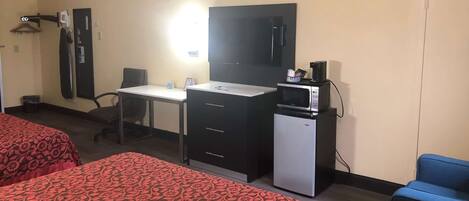 A hotel room with two beds, a desk, a chair, a small refrigerator, a microwave, and a TV.