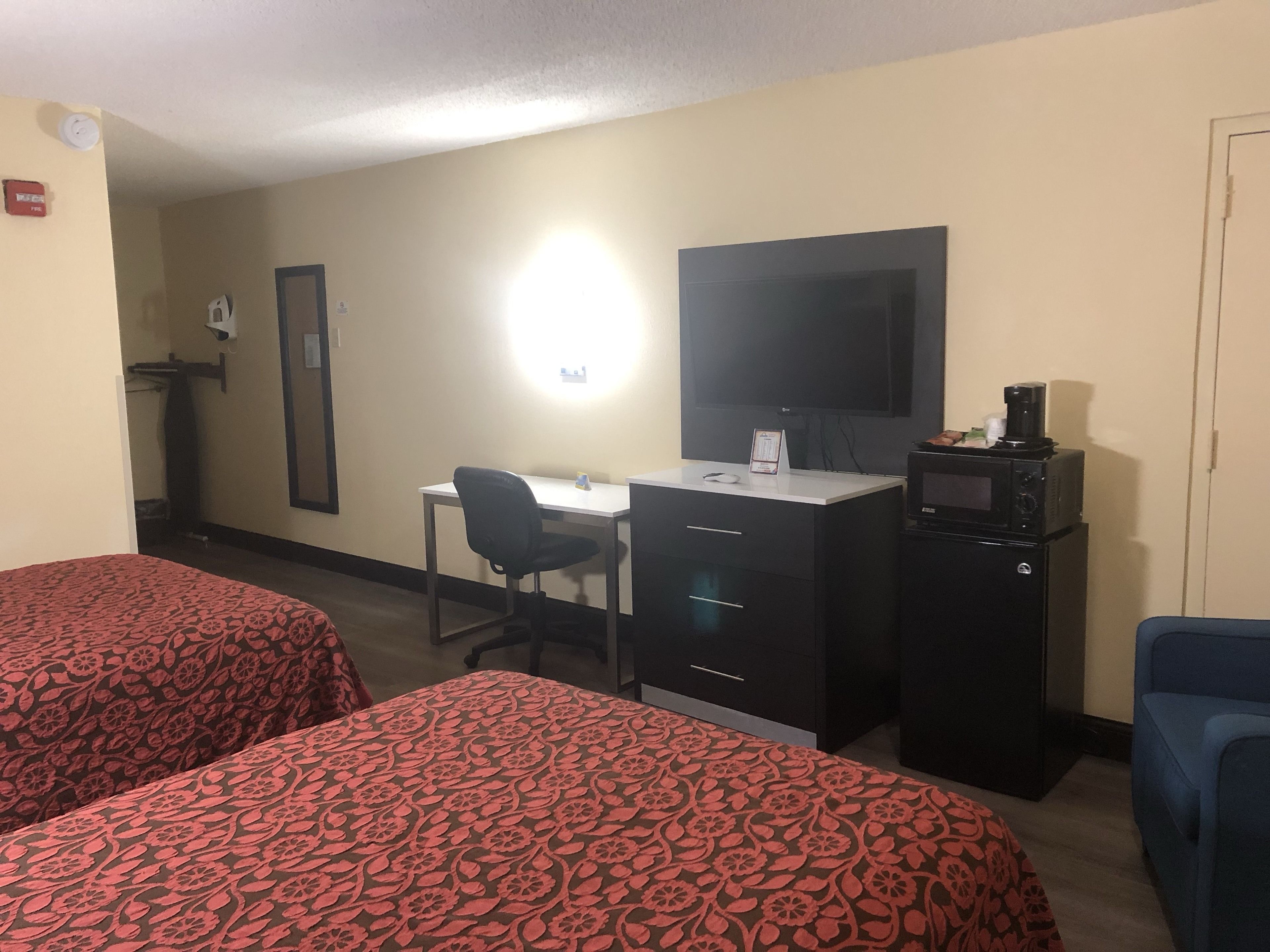 A hotel room with two beds, a desk, a chair, a TV, a microwave, and a small kitchenette.