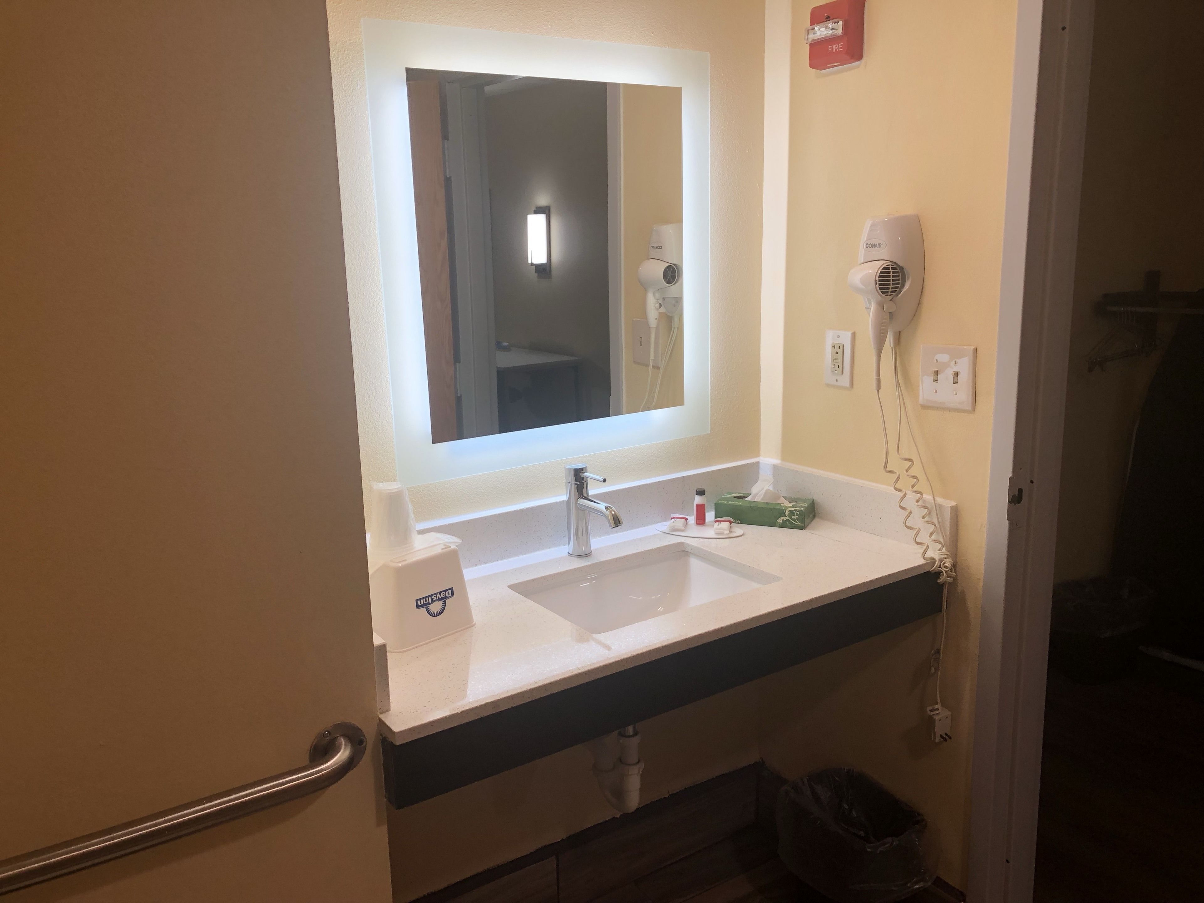 A bathroom with a white sink, a mirror, a hairdryer, and a trash bin.