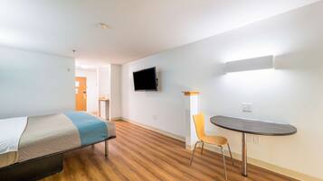 A hotel room with a bed, a small table, a chair, a TV mounted on the wall, and a wooden floor.