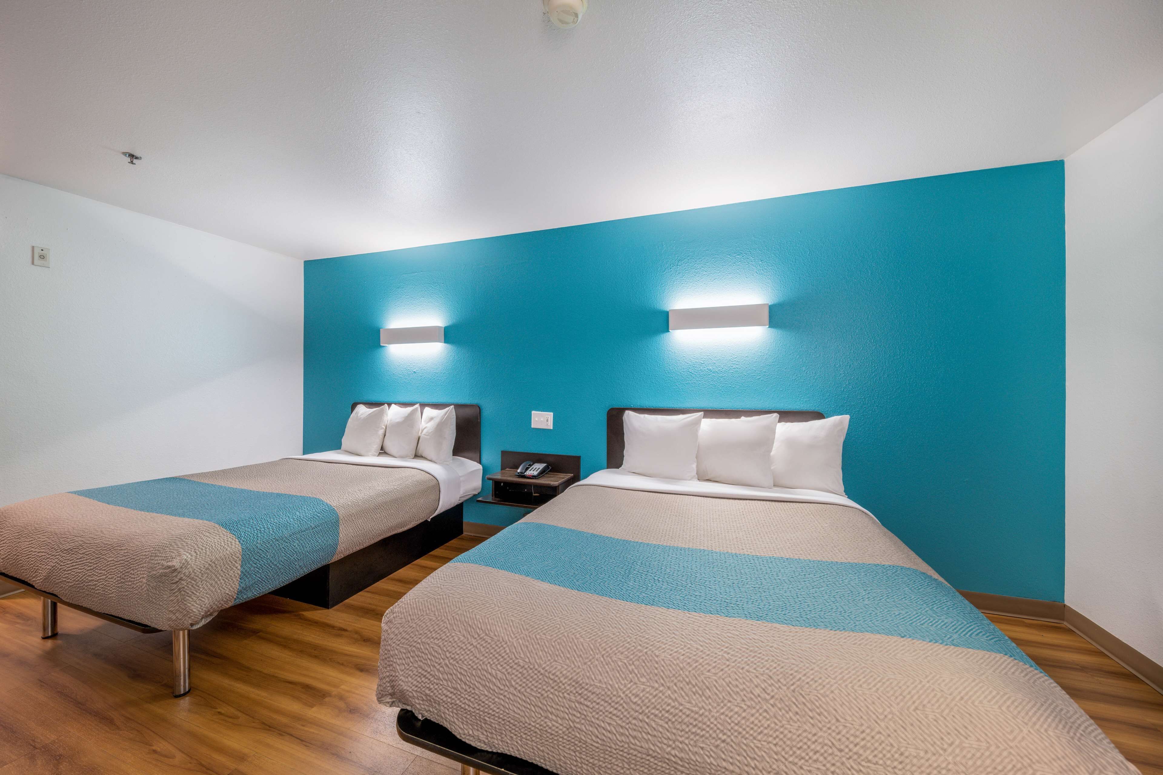Habitación de hotel con dos camas, piso de madera y una pared de acento azul.