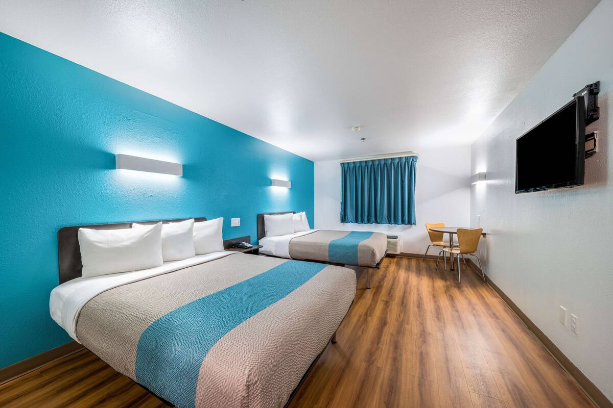 A hotel room with two beds, a desk, and a TV.