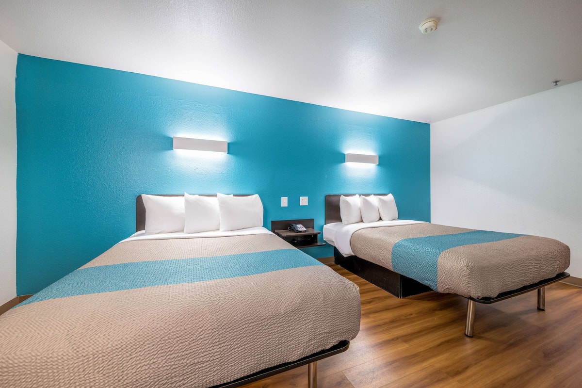 A hotel room with two beds, each with a headboard and pillows, and a nightstand with a phone.