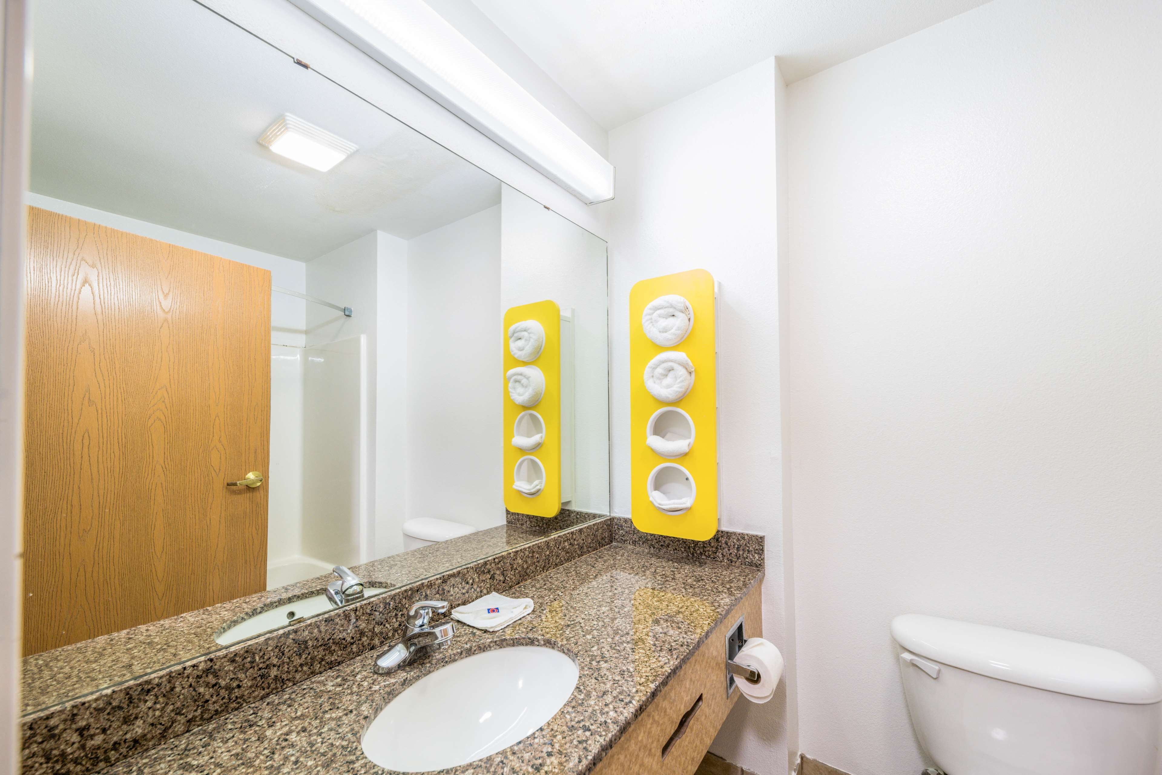 A bathroom with a granite countertop, a white sink, a mirror, and a toilet.