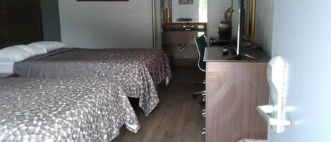 Una camera d'albergo con due letti, una scrivania, una sedia, uno specchio e un televisore.